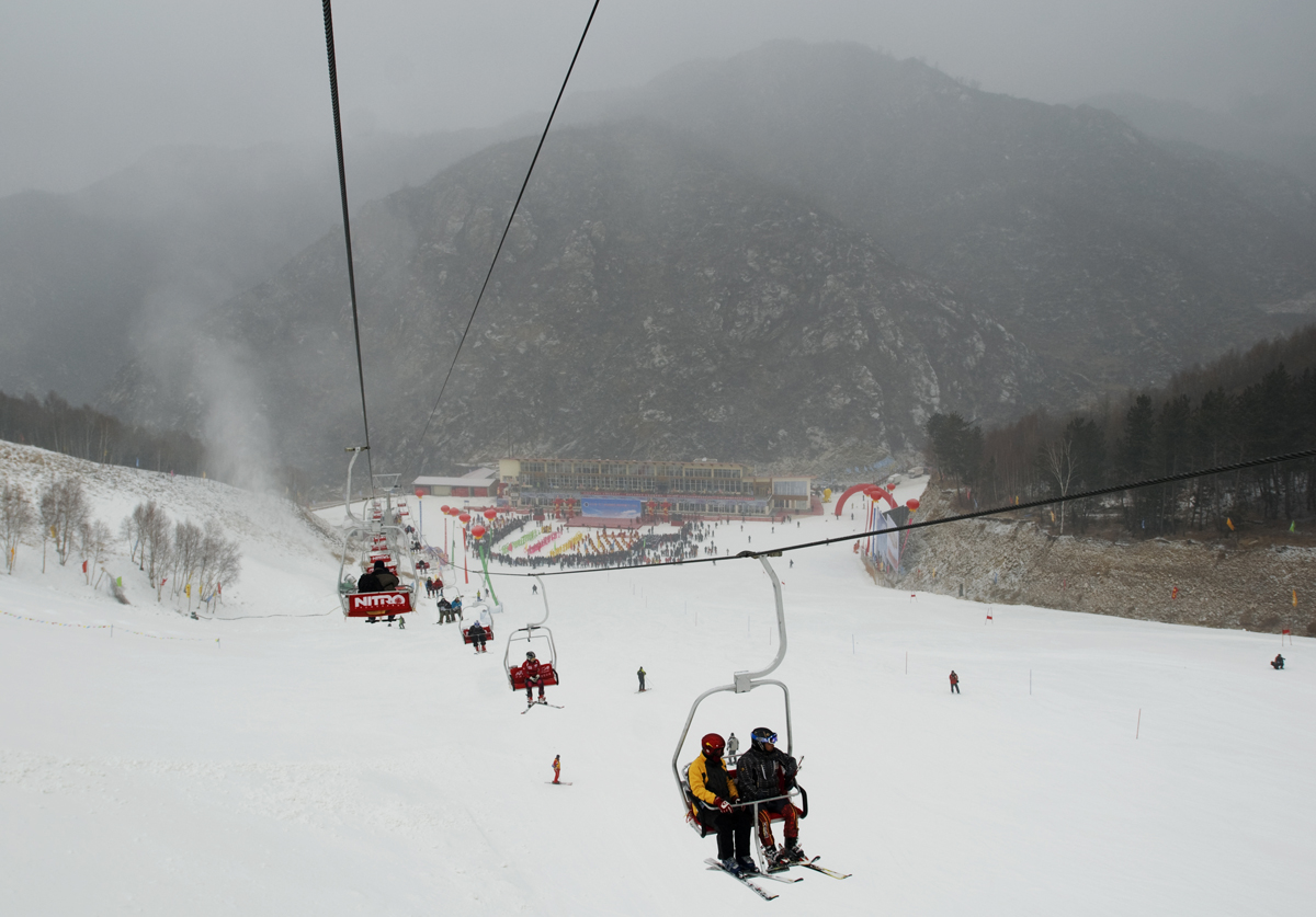 Historical photograph of skiers on a Wanlong chairlift, with the slopes and mountains beyond (2008)